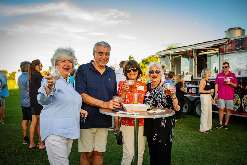 Four people at an outdoor event near a food truck, holding drinks and smiling.