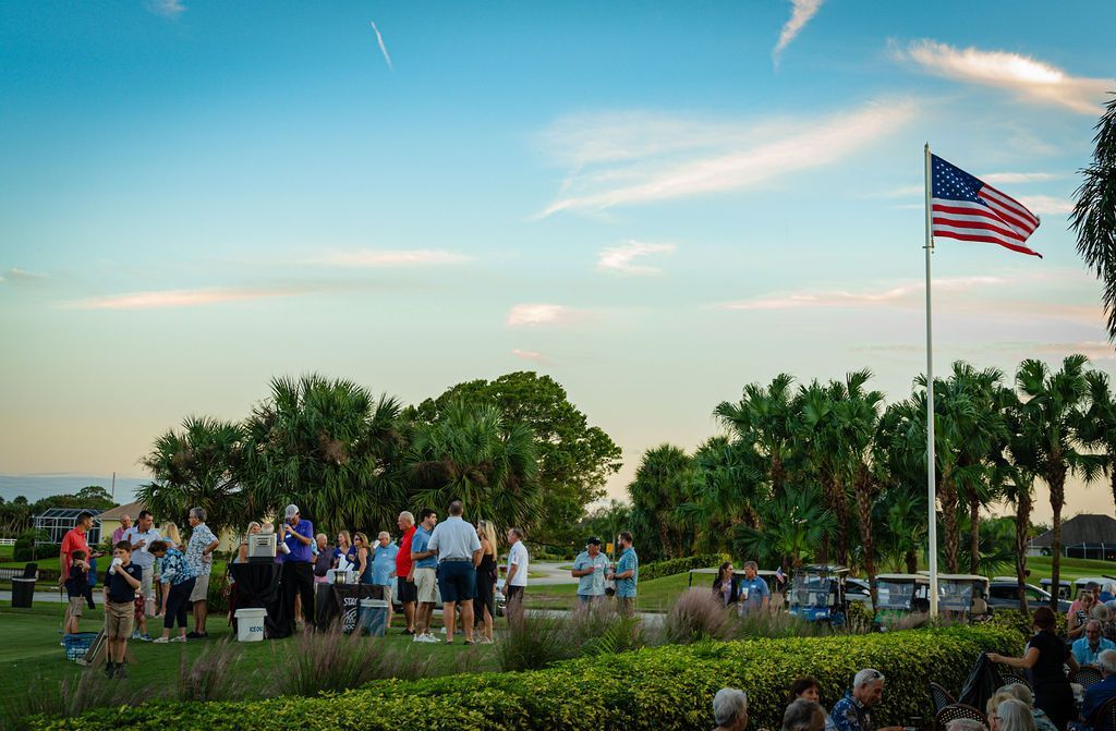 People gathered outdoors with an American flag; evening sky.