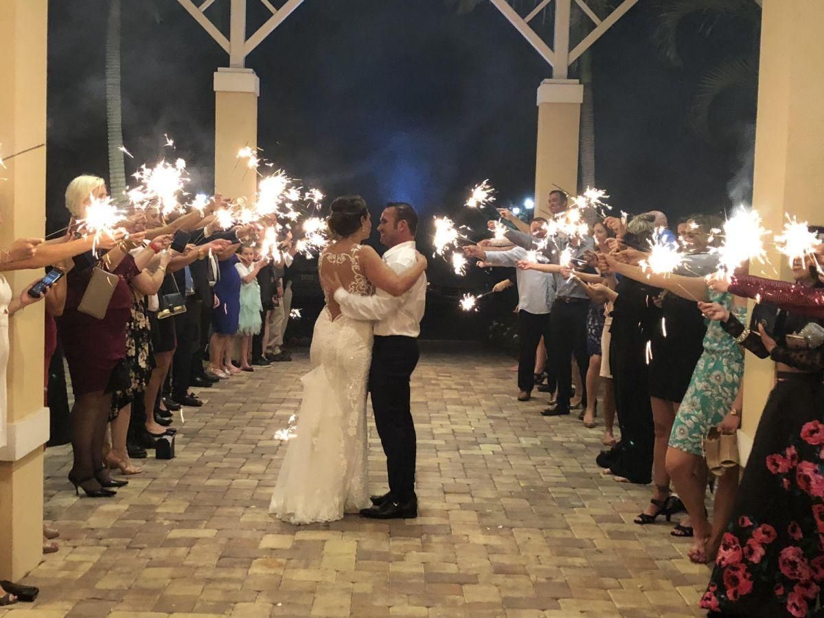Newlyweds surrounded by guests holding sparklers, celebrating at night.