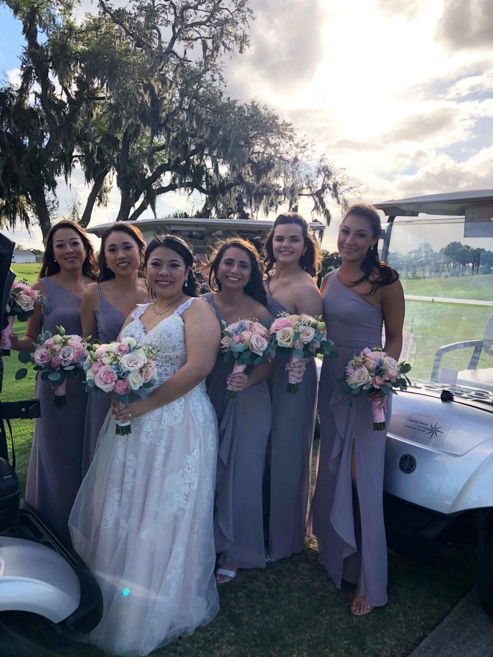 Bride with bridesmaids in lavender gowns holding bouquets, near golf cart.