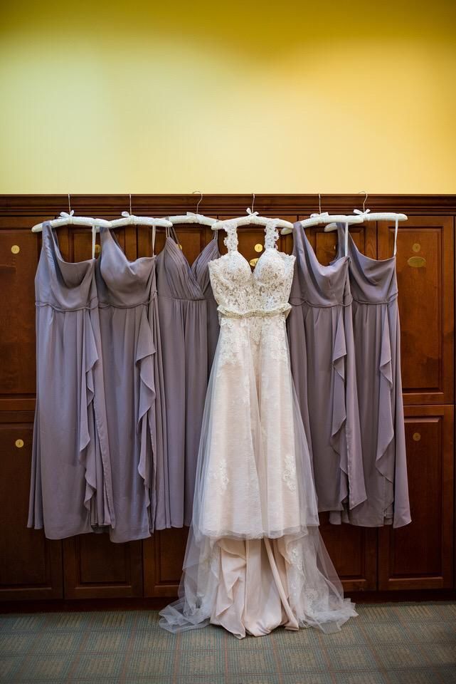 Wedding dress and bridesmaid dresses hanging on a wooden wall. Dresses are purple and light pink.