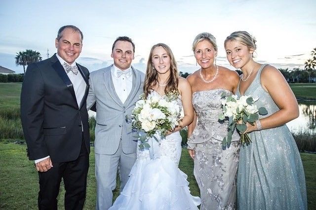 Wedding group: couple, family posing on golf course, smiles, holding bouquets, lakeside view.