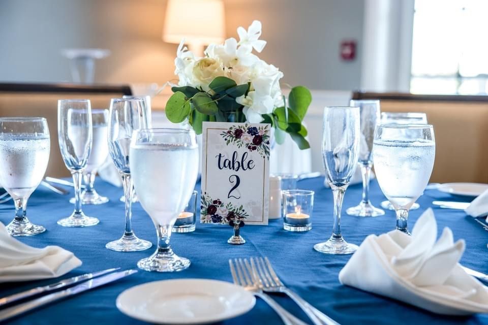 Wedding reception table with blue tablecloth, white flowers, and table number.