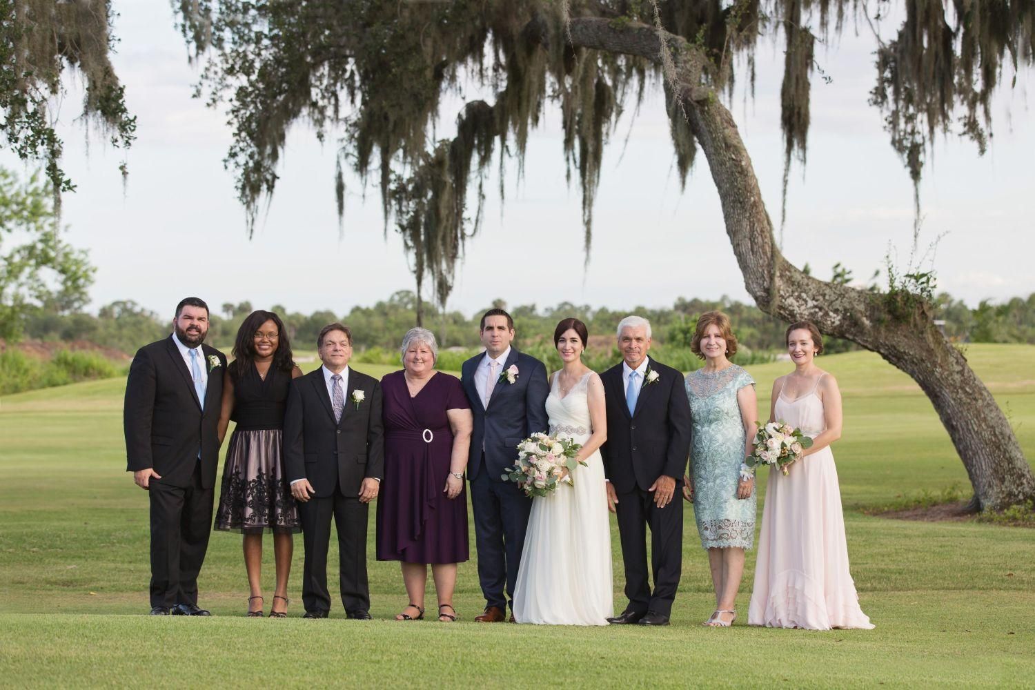 Wedding party posing in front of a tree on a golf course; a bride and groom are in the center.