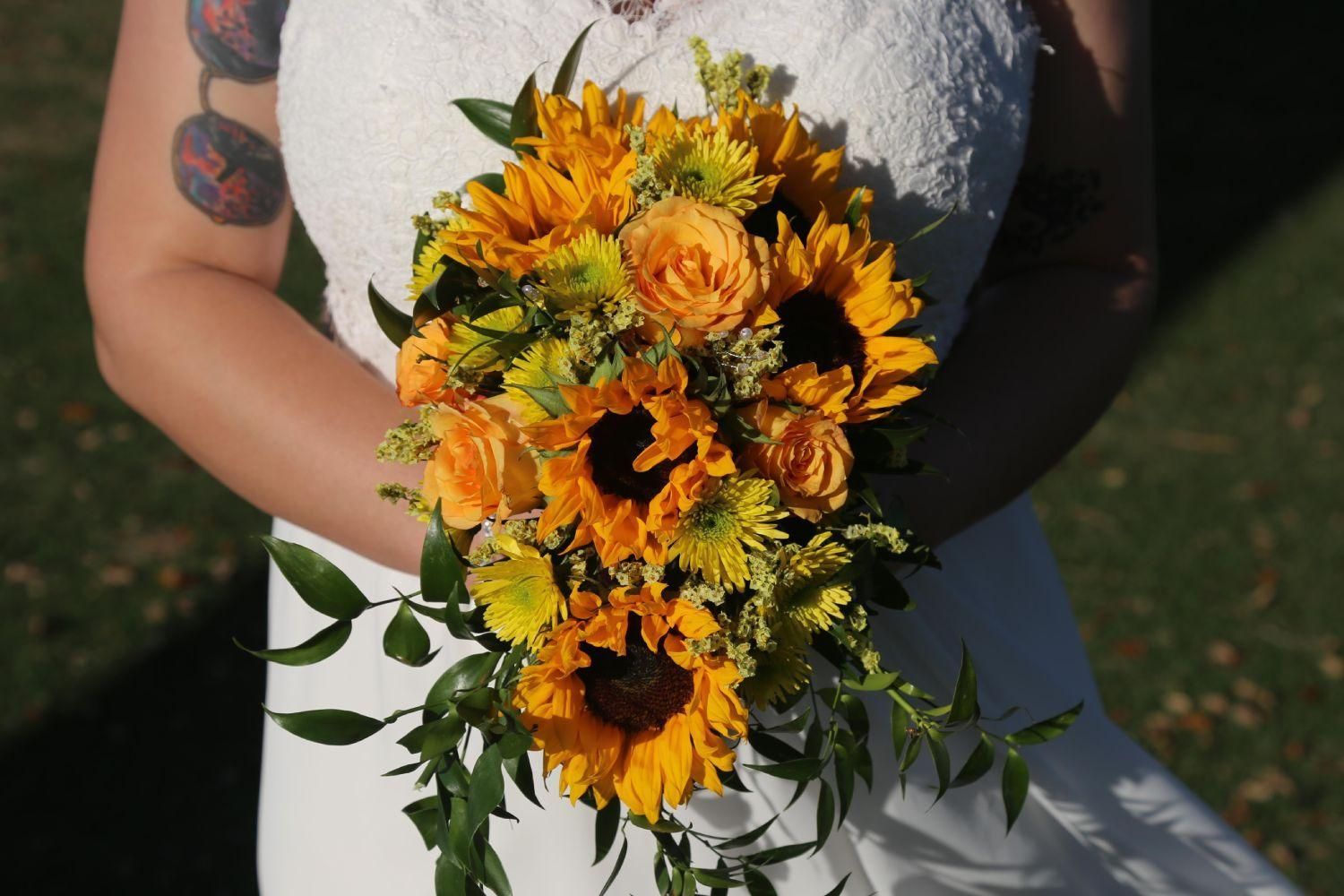 Bride holding a cascading bouquet of sunflowers and orange roses.