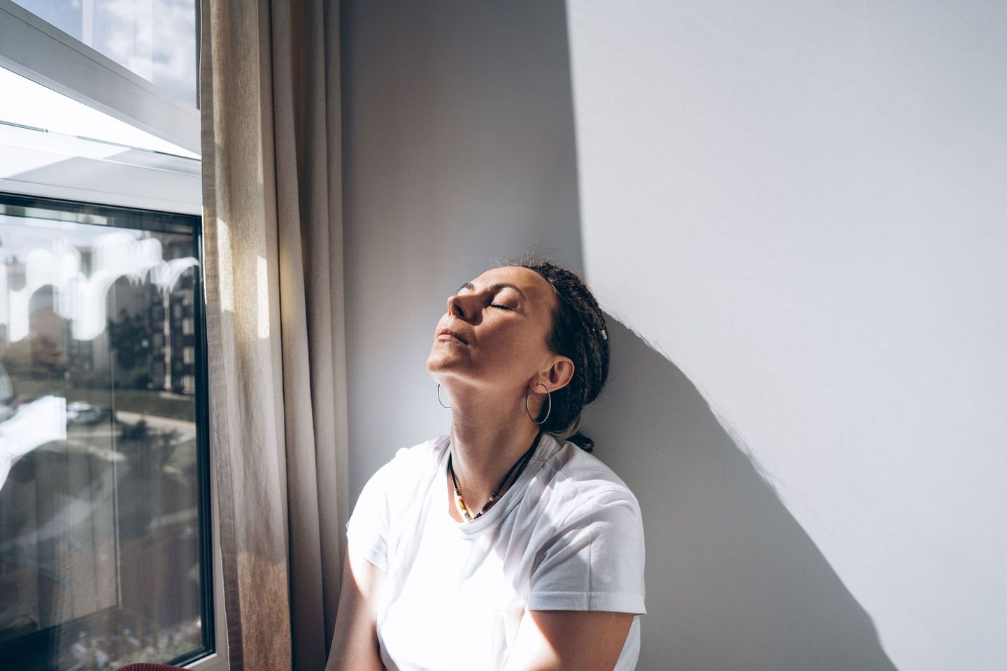 A woman is sitting in front of a window with her eyes closed.