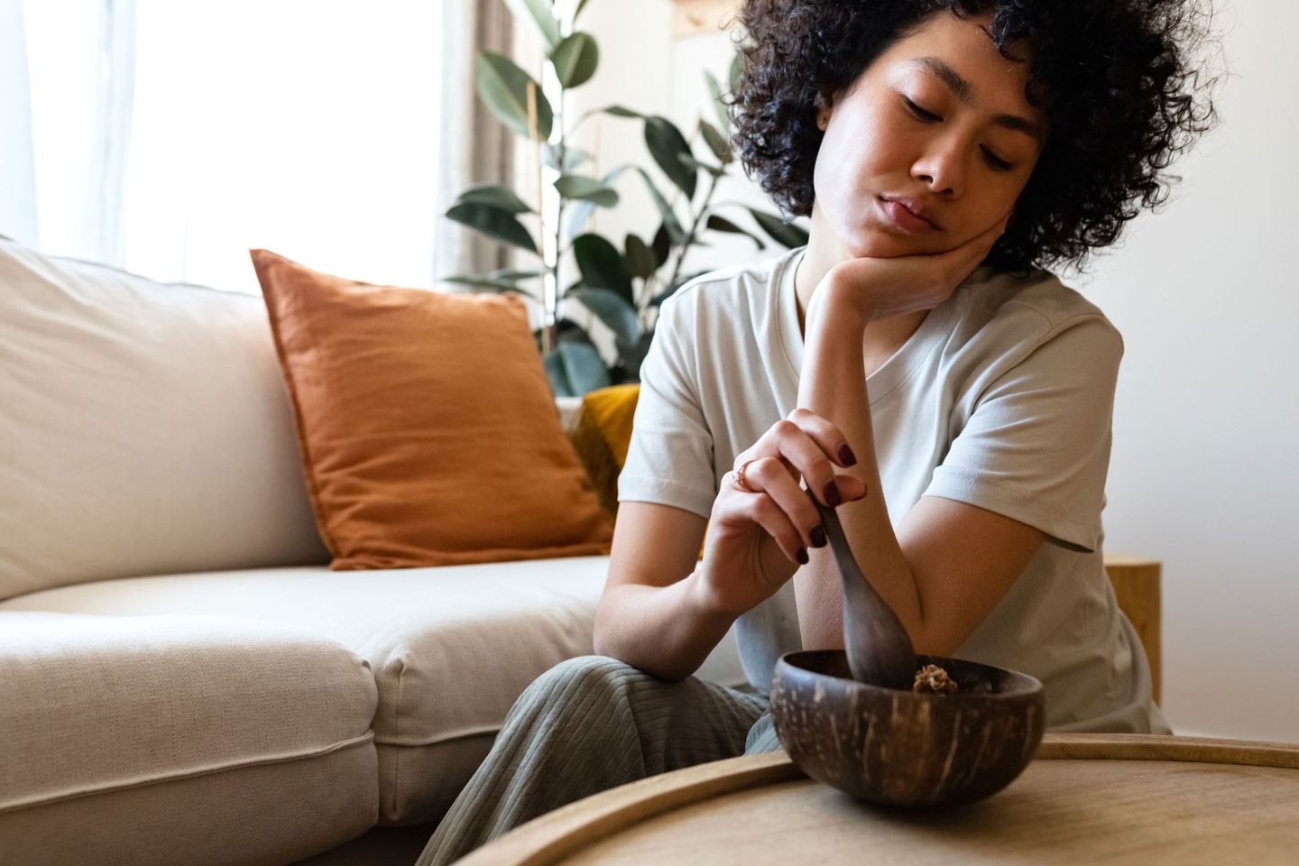 A woman is sitting on a couch looking at a bowl of food.