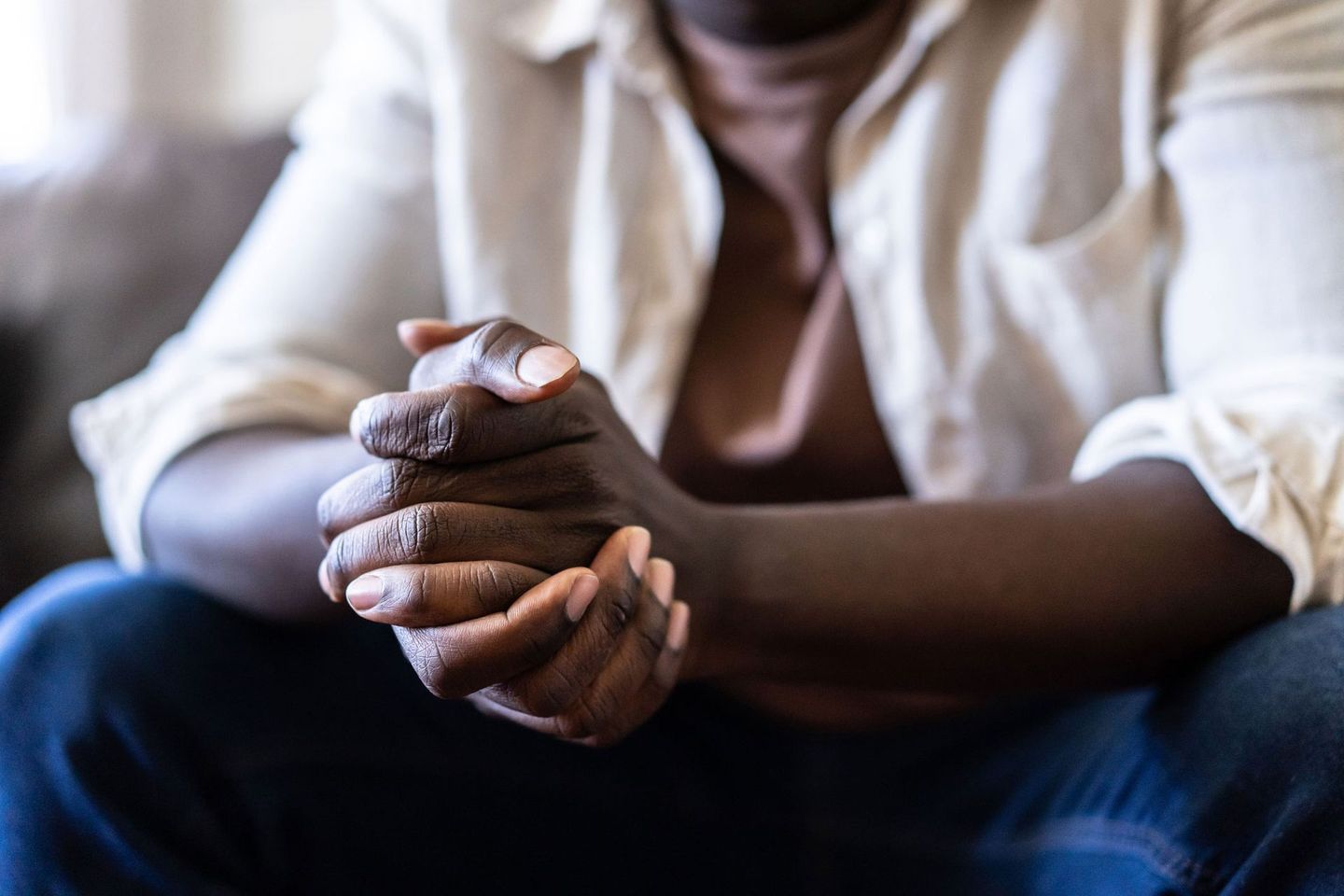 A man is sitting on a couch with his hands folded in prayer.