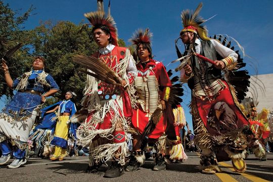 A group of people in native american costumes are marching down a street