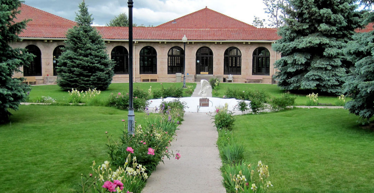 A building with a red roof is surrounded by trees and flowers