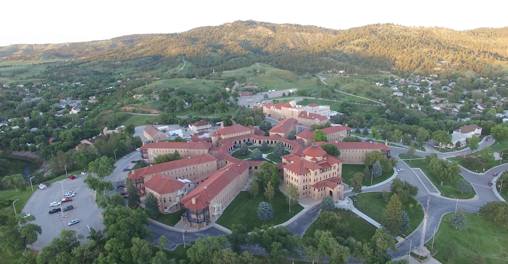 An aerial view of a large building surrounded by trees and mountains.