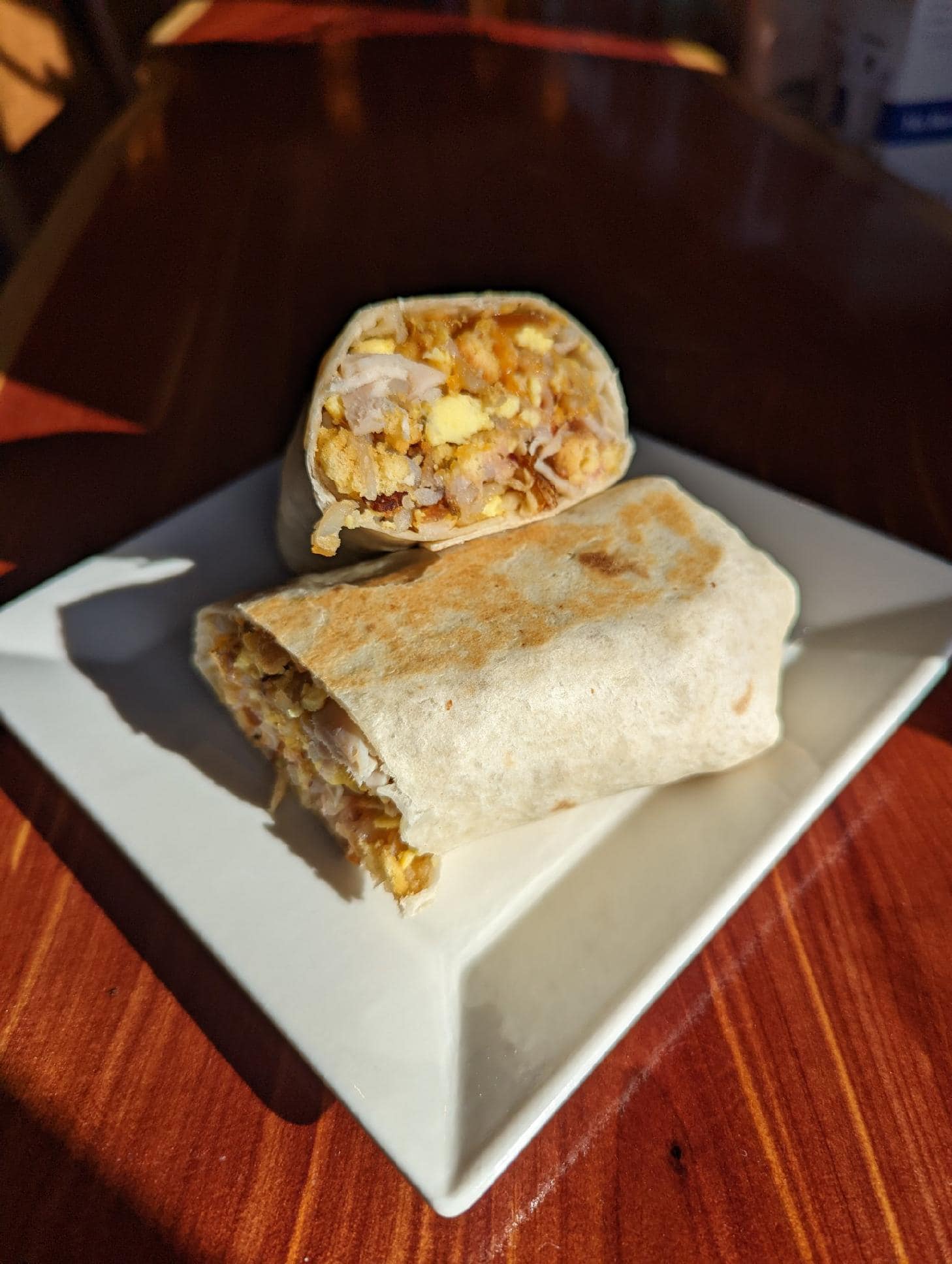 A burrito is cut in half on a white plate on a wooden table.