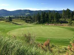 A golf course with a green and mountains in the background.
