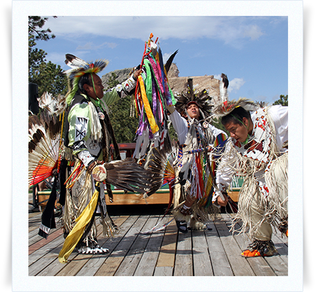 A group of men in native american costumes are dancing on a wooden deck