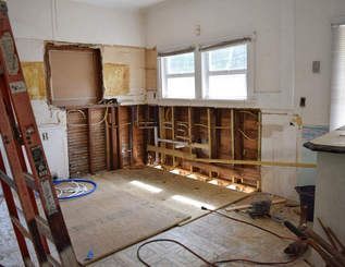 Kitchen renovation in progress: bare studs, exposed plumbing, partial demolition, ladder in foreground, window in background.