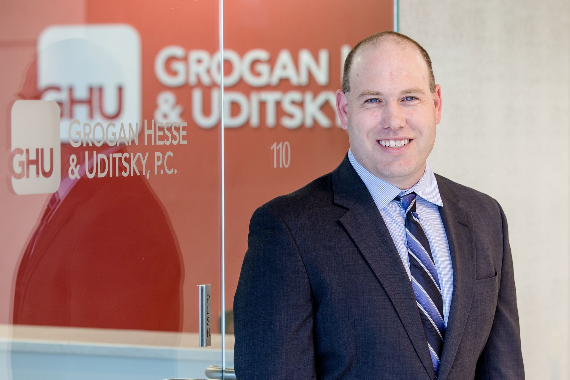 A man in a suit and tie is standing in front of a grogan & uditsky sign.