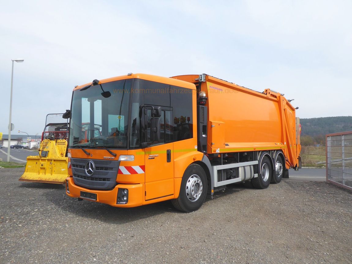 Ein orangefarbener Müllwagen steht auf einem Schotterplatz.