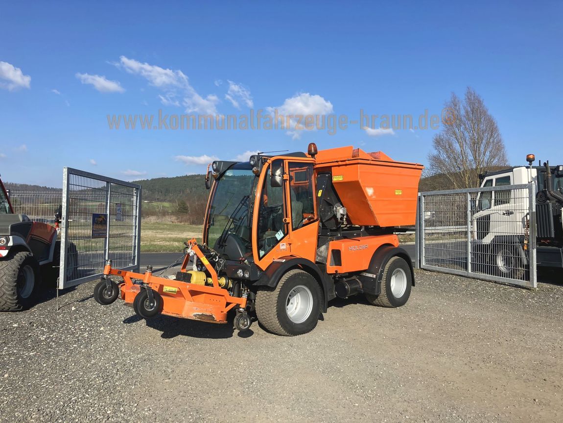 Ein orangefarbener Traktor steht auf einem Schotterplatz neben einem Zaun.