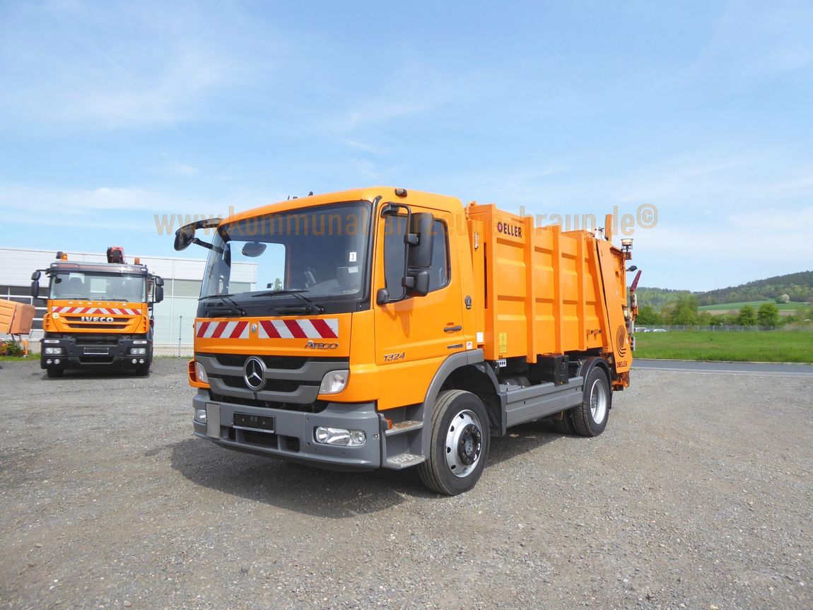 Zwei orangefarbene Müllwagen stehen auf einem Schotterplatz.