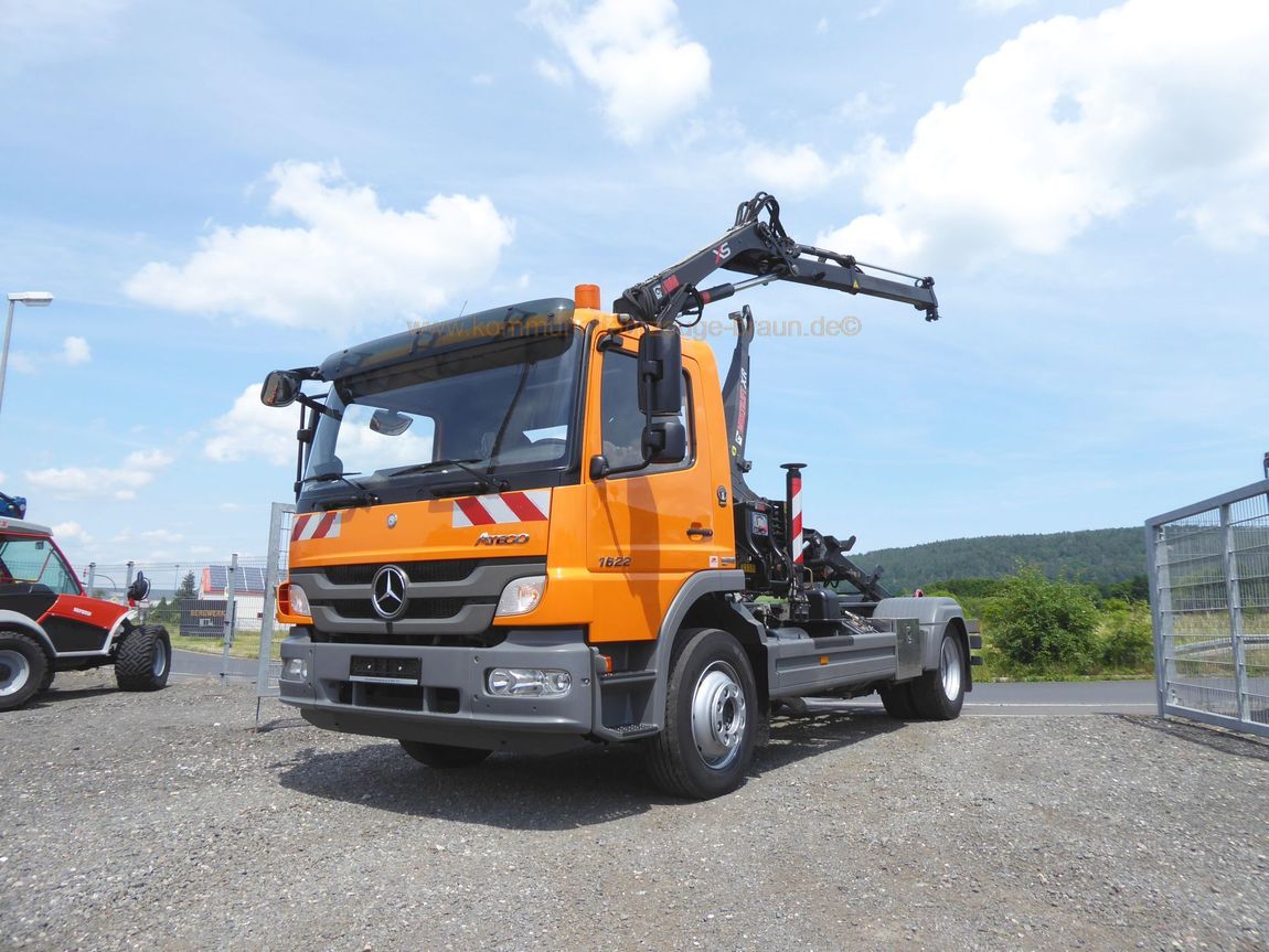 Ein orangefarbener Lastwagen mit einem Kran auf der Ladefläche steht auf einem Schotterplatz.