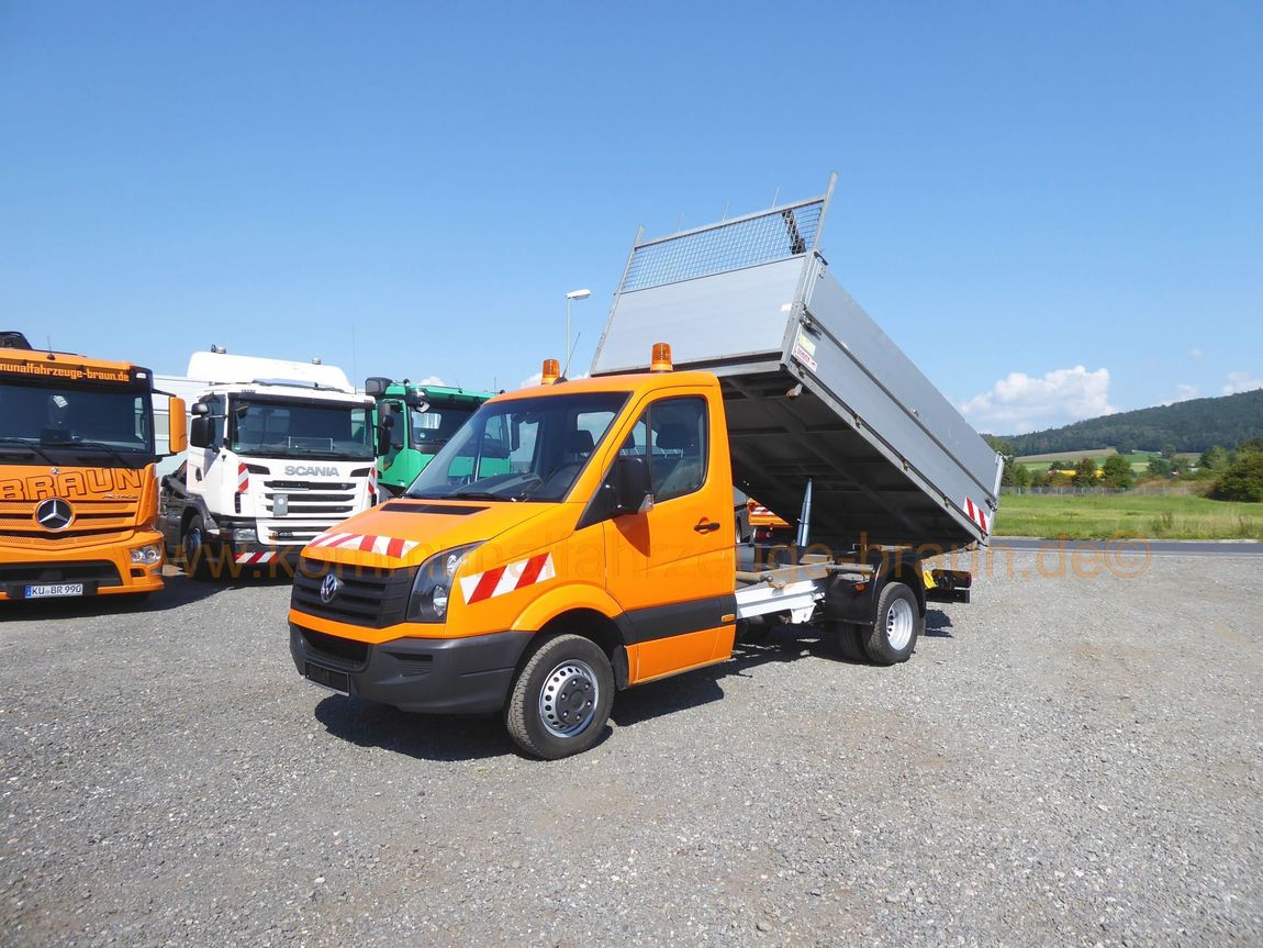 Ein orangefarbener Muldenkipper steht neben anderen Lastwagen auf einem Schotterplatz.