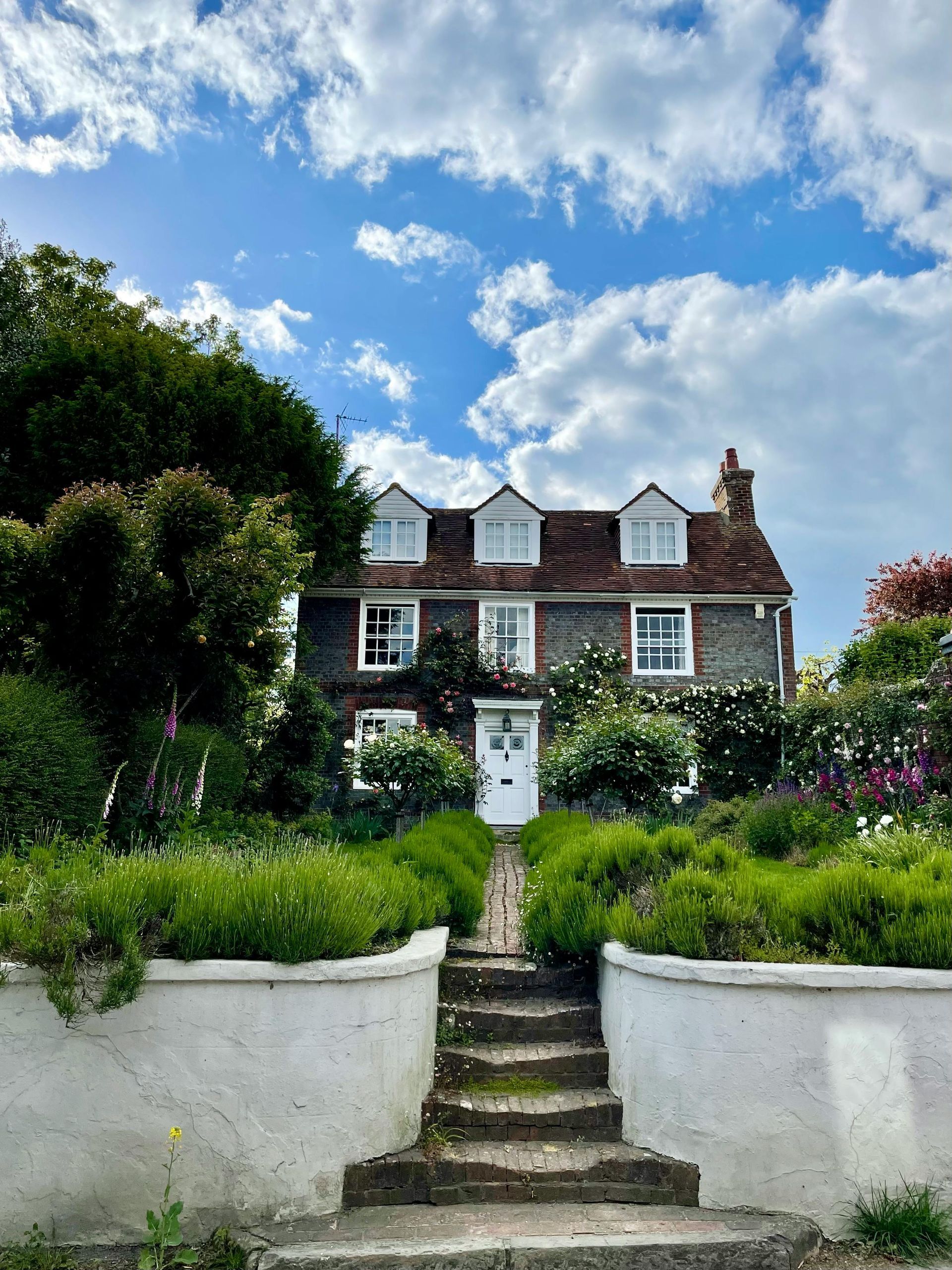 Two-story brick house with white trim and a garden path leading up to the front door under a cloudy sky.