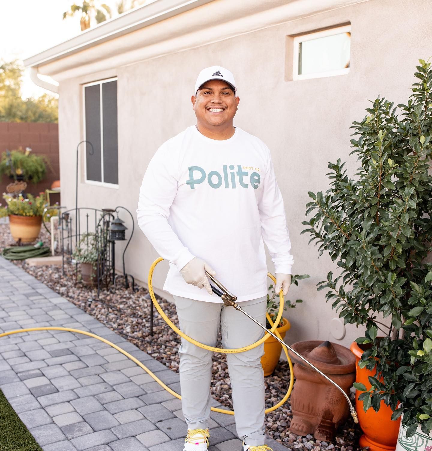 A man wearing a polite shirt is spraying plants with a hose