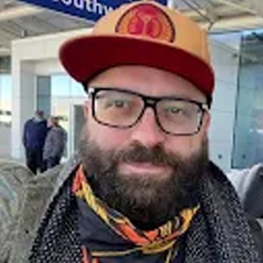 A man with a beard and glasses is wearing a hat and scarf.