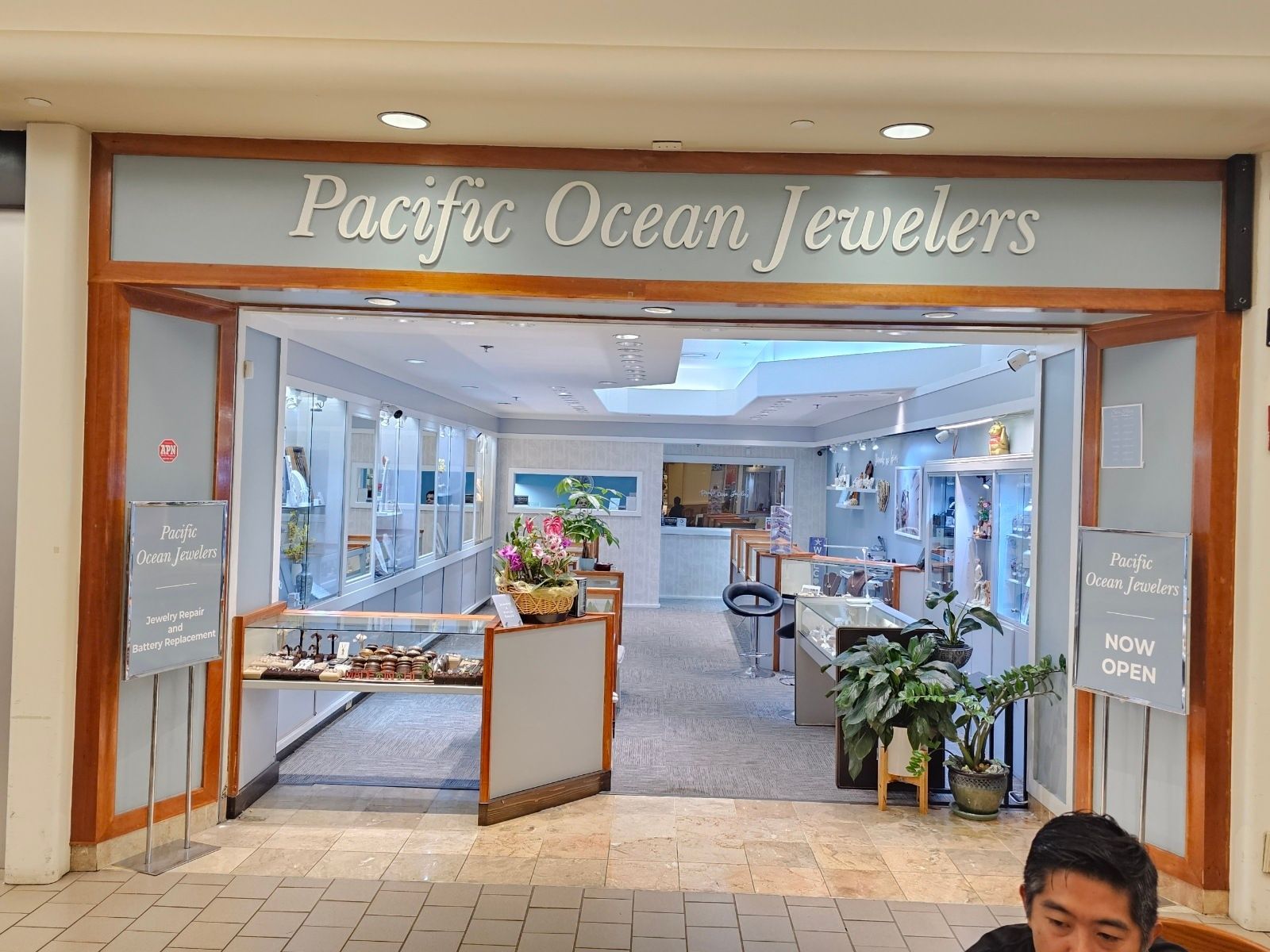 A man is sitting in front of a pacific ocean jewelers store.