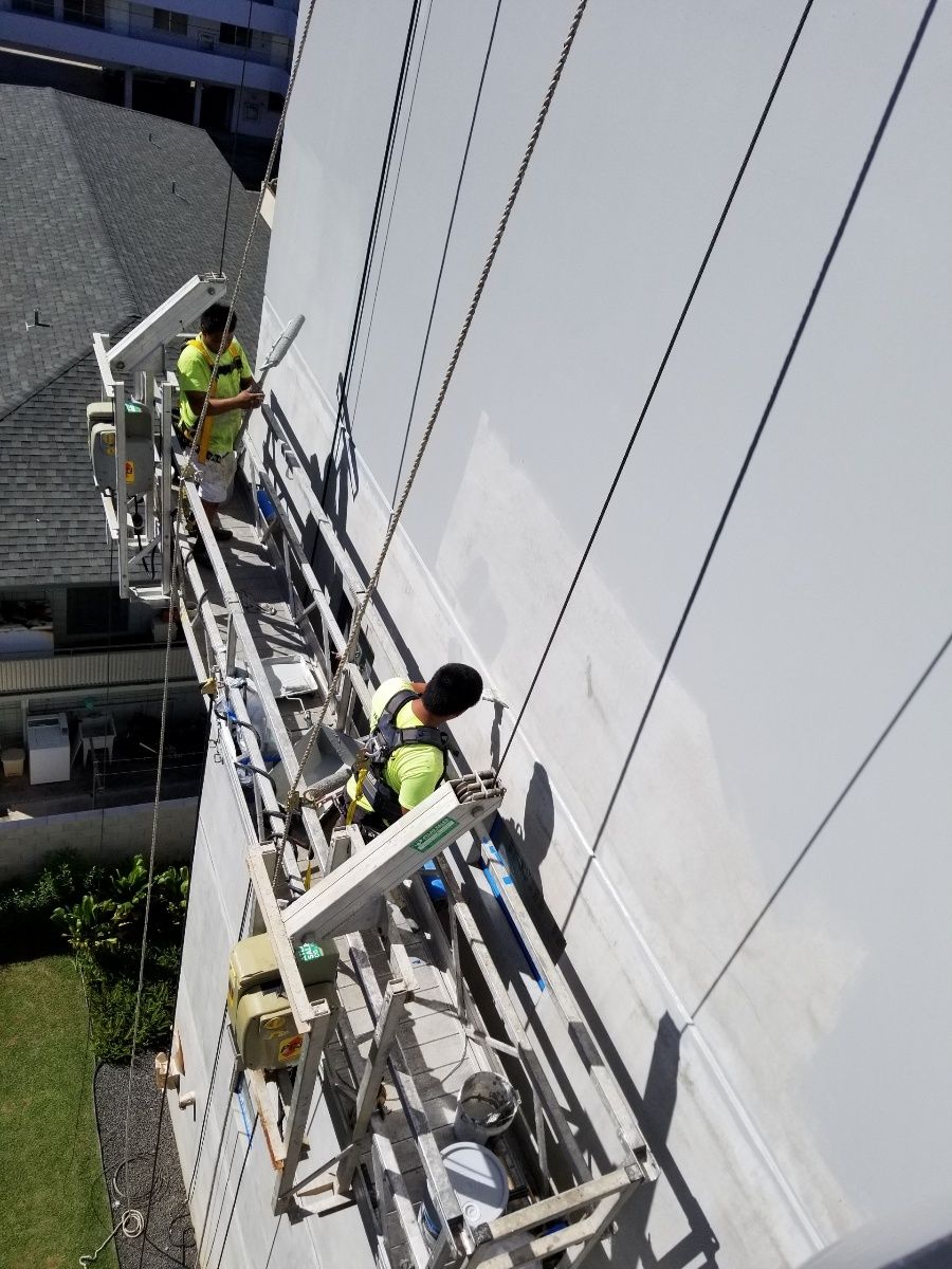 Two men are painting the side of a building on a scaffolding