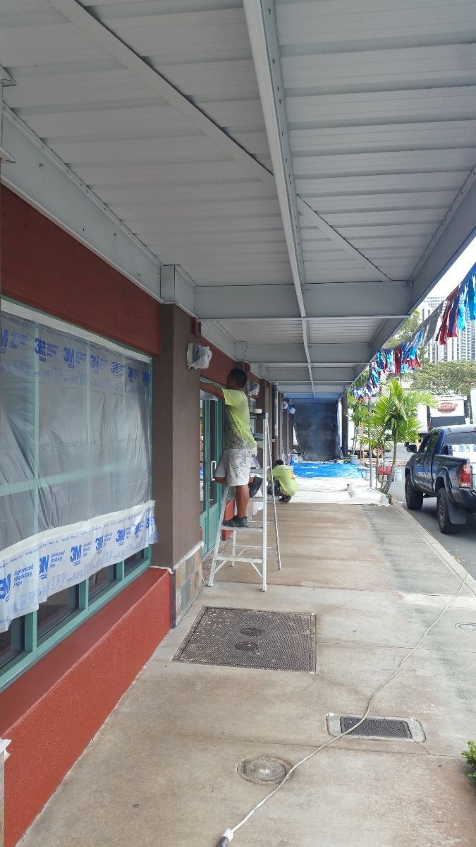 A man is standing on a ladder painting a building.