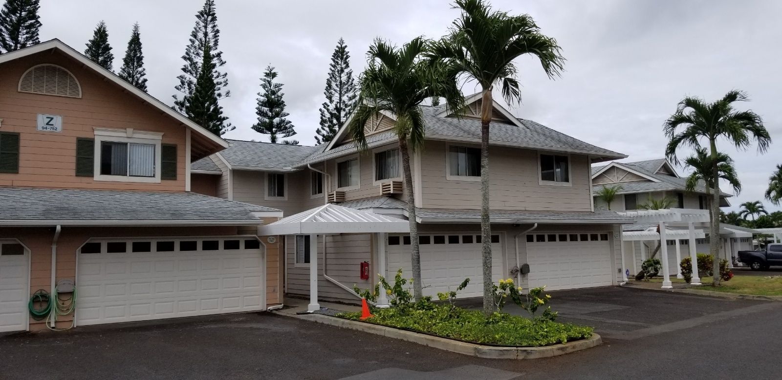 A row of houses with white garage doors and palm trees in front of them.