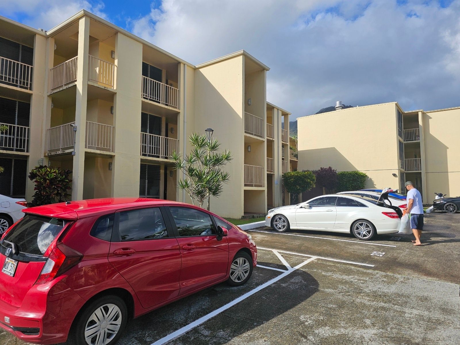 A red car is parked in a parking lot in front of a building.