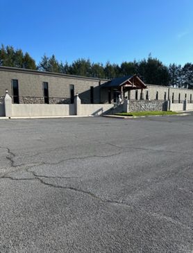 Gray brick building with a covered entrance, a paved parking lot, and a clear blue sky.
