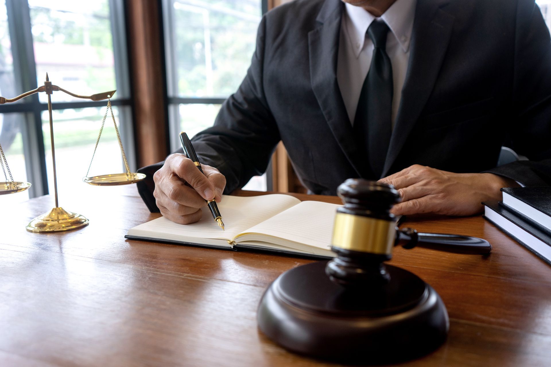 Person in suit writing, scales of justice and gavel on a wooden desk.
