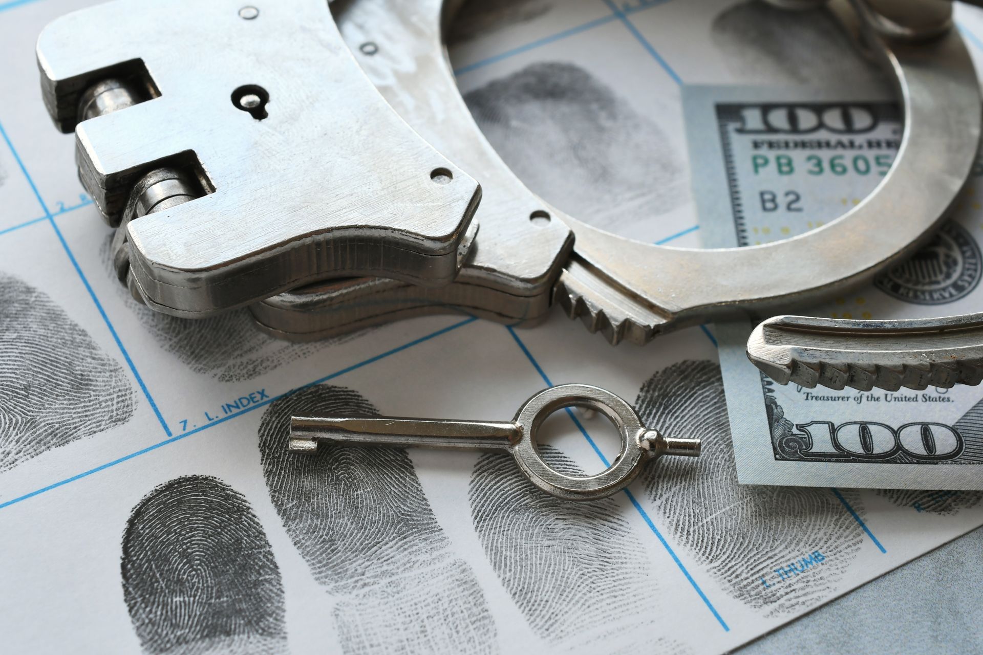 Handcuffs, key, and a section of a hundred-dollar bill rest on a fingerprint identification card.