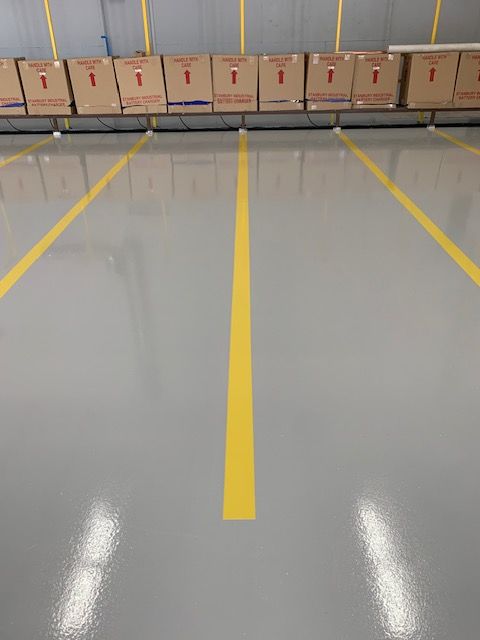 A row of cardboard boxes are lined up in a warehouse with a yellow line on the floor.