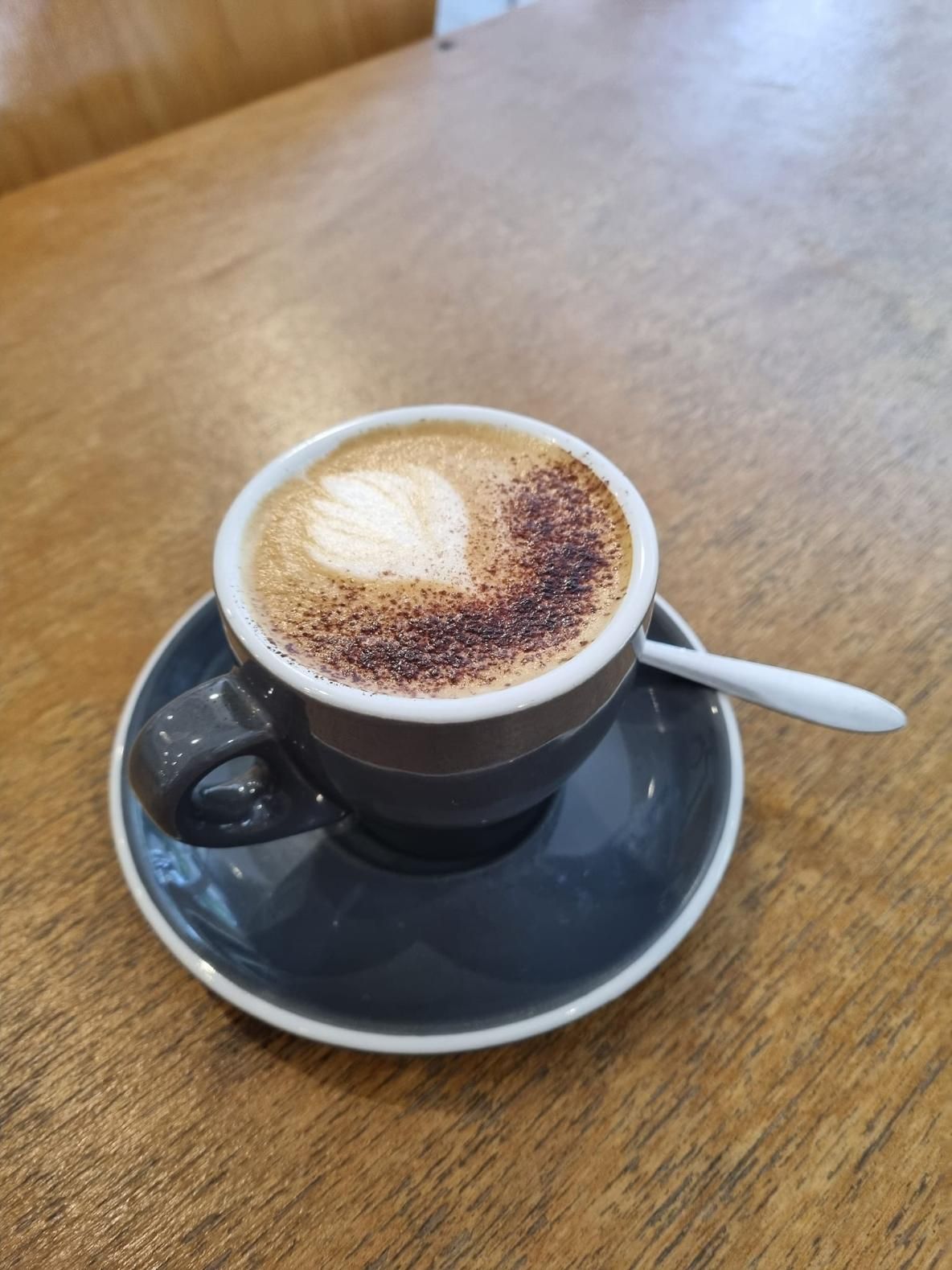 A Cup Of Cappuccino On A Saucer With A Spoon On A Wooden Table — Top Point Café In East Gosford, NSW