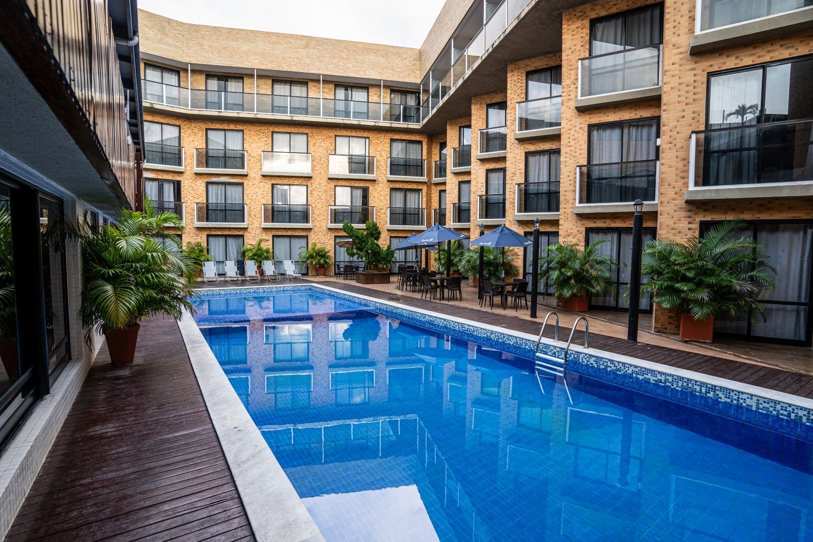 Piscina de hotel no pátio com água azul, rodeada por edifícios de tijolo e vasos de plantas.
