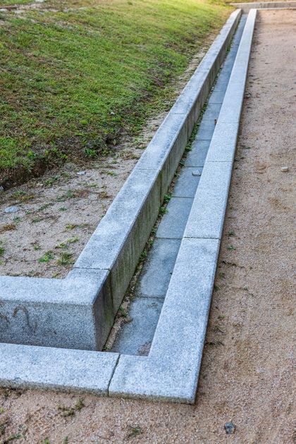 A stone drain is sitting on the side of a dirt road next to a grassy field.