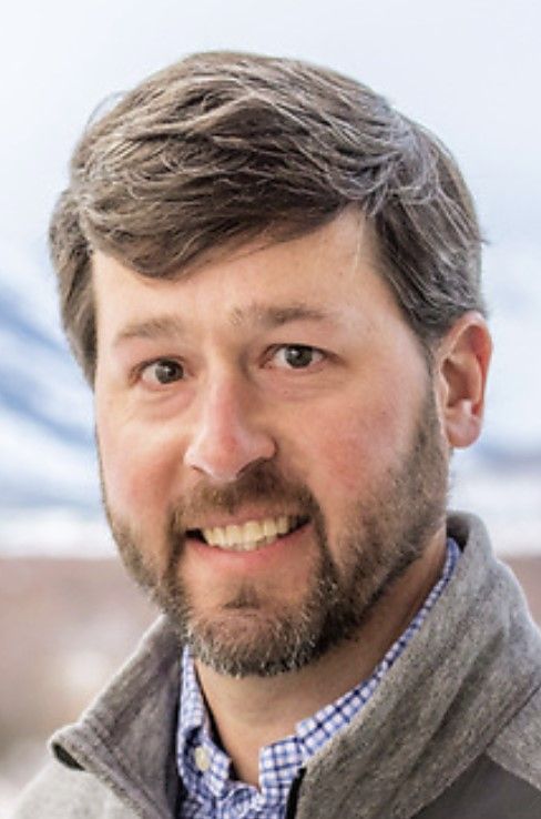 a man with a beard and a gray jacket is smiling for the camera .