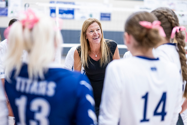 a group of volleyball players are standing around a coach on a court .