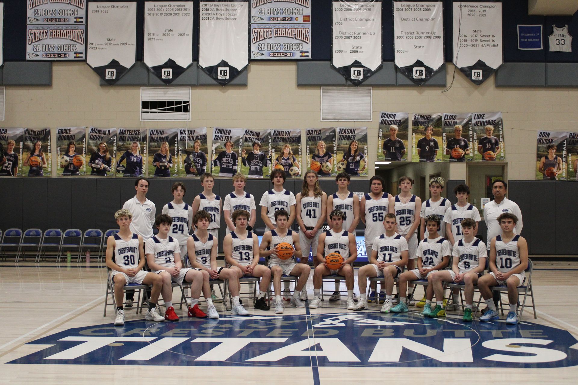 A basketball team poses for a team photo in front of a titans logo on the floor.
