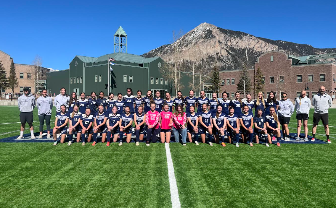 a group of girls are playing soccer on a field with mountains in the background .