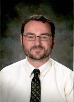 A man with a beard and glasses is wearing a white shirt and tie.
