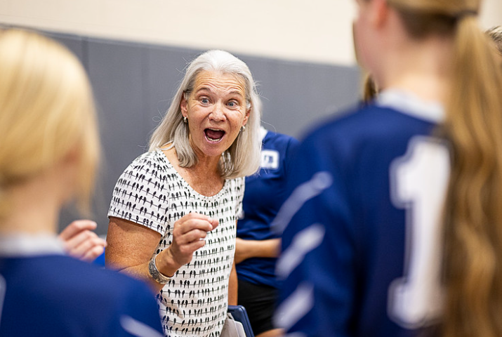 a woman is talking to a group of volleyball players in a gym .