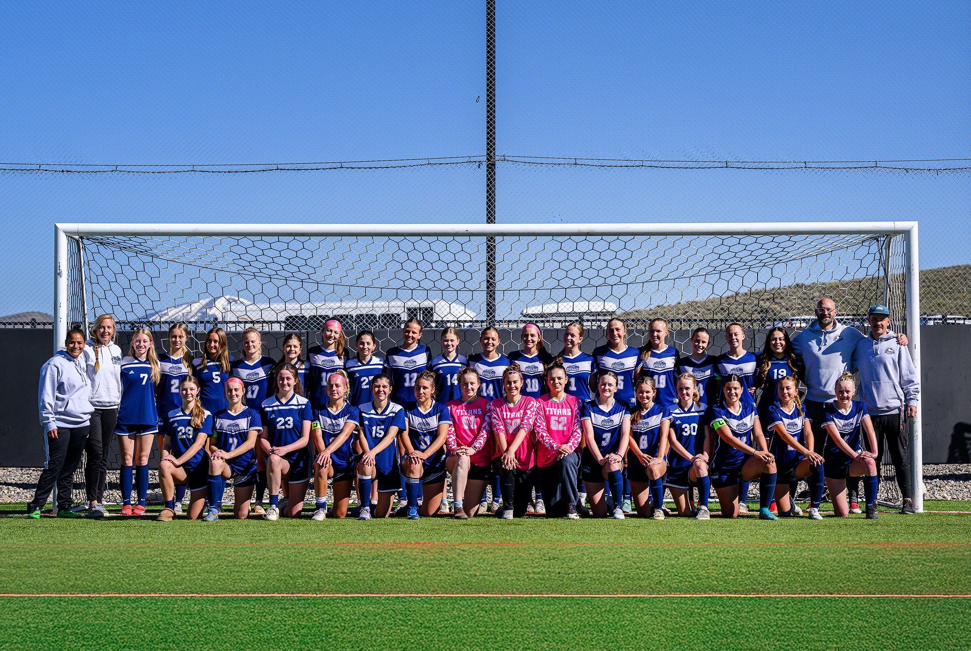 a group of girls are playing soccer on a field with mountains in the background .
