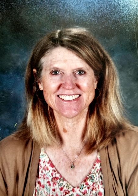 a woman wearing a brown cardigan and a floral shirt is smiling for the camera .