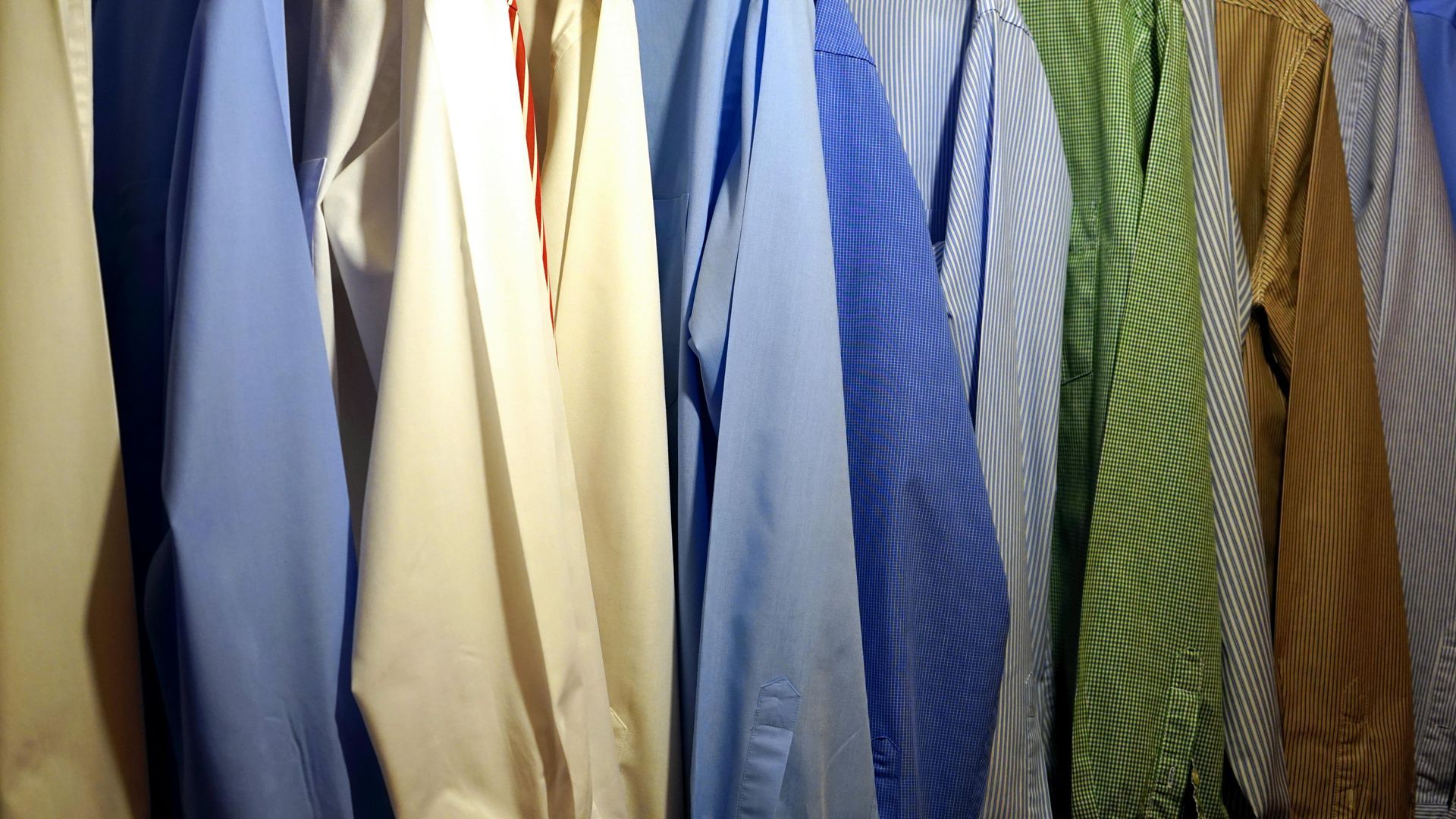 A row of shirts and ties are hanging on a rack.