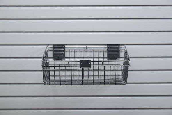 A wire basket is hanging on a slat wall.